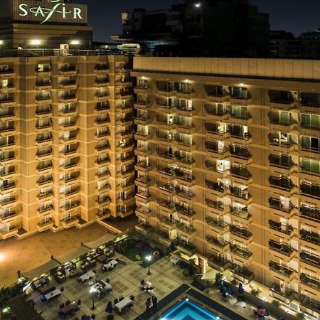 Safir Hotel Cairo Giza Ngoại thất bức ảnh The photo shows a multi-story hotel building at night. The building is illuminated, showcasing multiple balconies along its facade. In front of the hotel, there is an outdoor area with seating arranged around a pool, which is also lit up. The hotel's