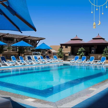 Safir Hotel Cairo Giza Ngoại thất bức ảnh The photo showcases a bright, inviting swimming pool surrounded by lounging chairs. The pool is set in a sunny outdoor area, with clear blue water reflecting the sky. There are several blue umbrellas providing shade over the lounge chairs, which are 