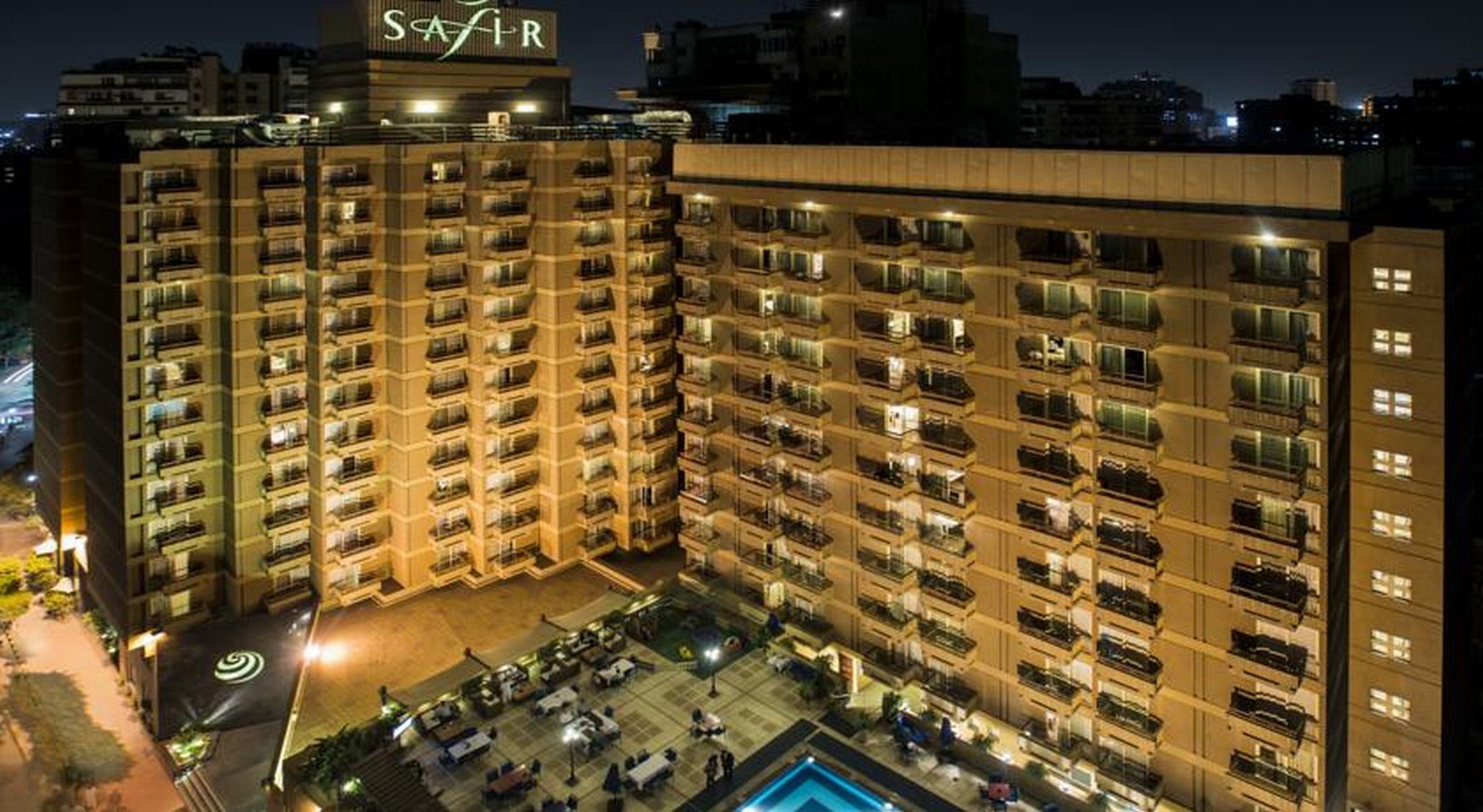 Safir Hotel Cairo Giza Ngoại thất bức ảnh The photo shows a multi-story hotel building at night. The building is illuminated, showcasing multiple balconies along its facade. In front of the hotel, there is an outdoor area with seating arranged around a pool, which is also lit up. The hotel's