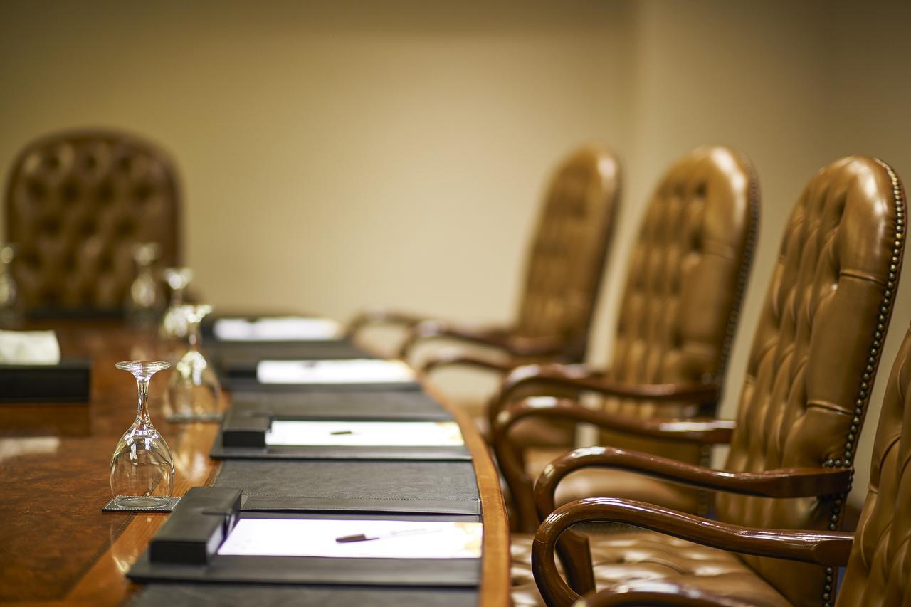 Safir Hotel Cairo Giza Ngoại thất bức ảnh The photo shows a conference room setting with a long wooden table and several high-backed chairs. The chairs appear to be upholstered in a brown leather material. Each place at the table has a black folder or pad, and there are also glass water gobl