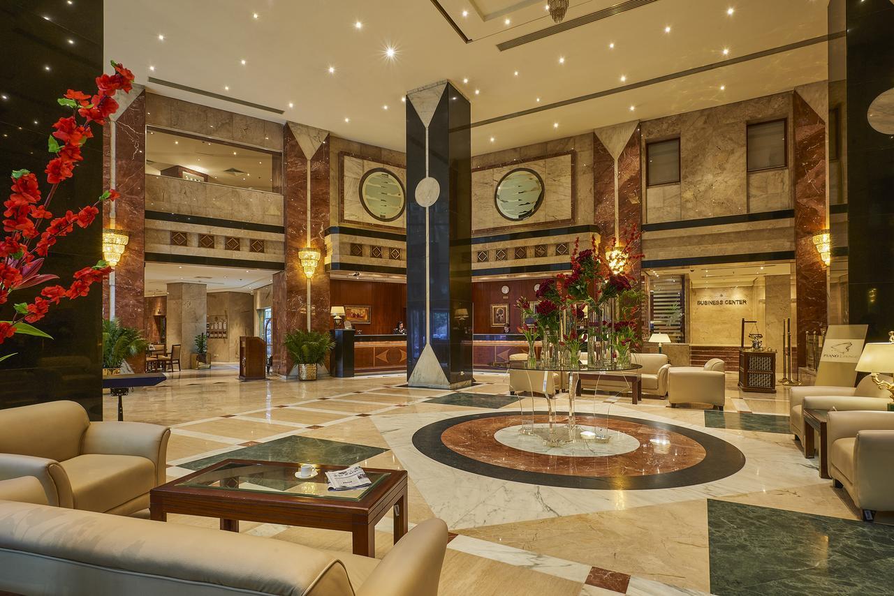 Safir Hotel Cairo Giza Ngoại thất bức ảnh The photo shows a luxurious hotel lobby. The space features elegant marble flooring with a circular design at the center. There are comfortable seating arrangements with light-colored sofas and wooden coffee tables. Lush green plants and vibrant flor