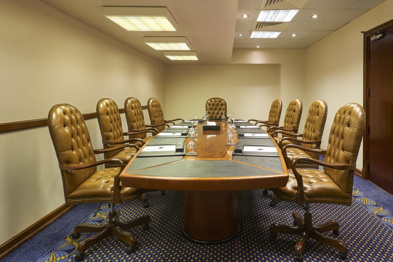 Safir Hotel Cairo Giza Ngoại thất bức ảnh The photo shows a conference room with a large oval table surrounded by several brown leather chairs. There are eight chairs in total, each with a high back and wheels. The table has some notepads and glasses of water set up on it. The room has neutr