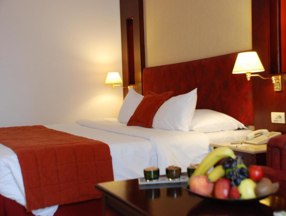 Safir Hotel Cairo Giza Phòng bức ảnh The photo shows the interior of a hotel room featuring two beds with white bedding and an orange throw blanket. There are decorative pillows on the beds. The walls are designed in warm tones, and there are two bedside lamps providing soft illuminatio