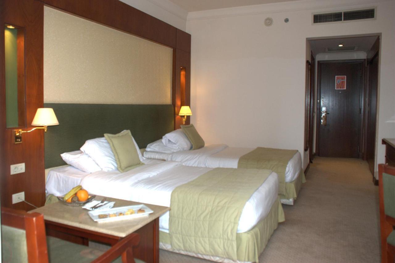 Safir Hotel Cairo Giza Phòng bức ảnh The photo shows a hotel room featuring two single beds with light green bedspreads and white linens. There are bedside lamps on either side of the beds, and the headboard has a soft, textured design. A small seating area is visible with a wooden chai